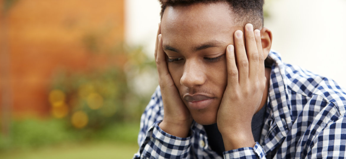 Depressed young black man with head in hands, close up, head and shoulders